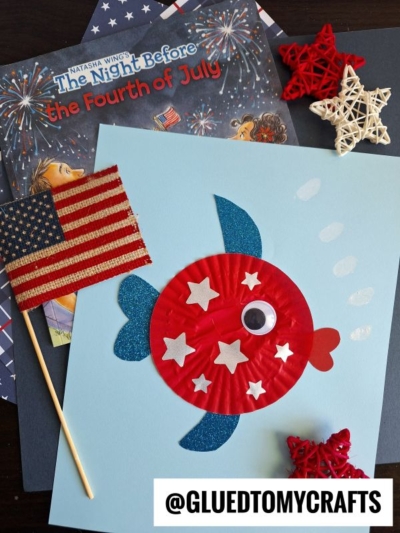 A children’s Fourth of July craft scene featuring a blue paper fish decorated with red and white cupcake liners, stars, a googly eye, and a flag joins other 4th of July crafts like patriotic star ornaments and the book The Night Before the Fourth of July.