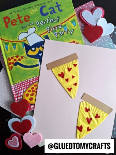 A children's book titled Pete the Cat and the Perfect Pizza Party sits beside adorable pete the cat crafts—handmade pizza slices decorated with red heart shapes, surrounded by colorful heart-shaped felt cutouts. The handle @GLUEDTOMYCRAFTS is at the bottom.