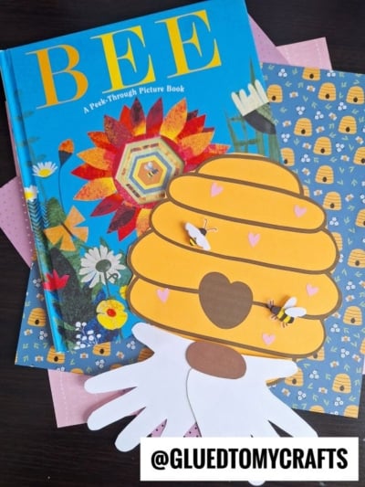 A children’s book titled BEE lies on patterned paper with bees and beehives, next to a charming Paper Beehive Gnome craft adorned with bees and heart decorations. @GLUEDTOMYCRAFTS is written at the bottom.