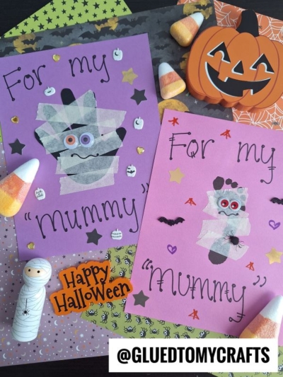 Two Halloween crafts on purple and pink paper read For my mummy, each with a cute mummy made from gauze, googly eyes, and decorations. Surrounding are Halloween items like a pumpkin, candy corn, stickers, and a “Happy Halloween” sign.