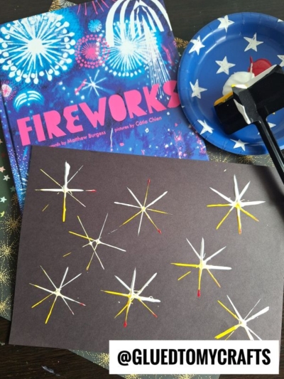 A book titled Fireworks, a star-patterned plate with a paint roller, and black paper decorated with painted firework designs—perfect inspiration for 4th of July crafts. The handle @GLUEDTOMYCRAFTS appears at the bottom.