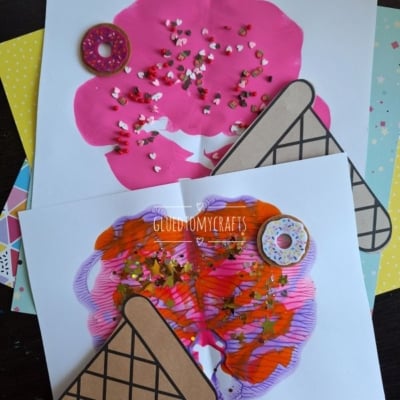 Two pieces of paper display colorful ice cream cone art made with paint and sprinkles. One has a melted ice cream effect with pink paint; the other features pink and orange swirls. Both have paper cone cutouts and are decorated with fake donuts.