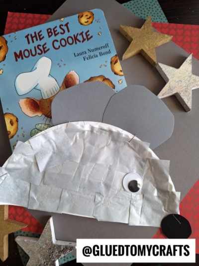 A children’s book titled “The Best Mouse Cookie” sits next to a mouse craft made from paper, tissue, and a googly eye—perfect for summer craft ideas. Gold and silver star decorations surround the items. The text @GLUEDTOMYCRAFTS appears at the bottom.