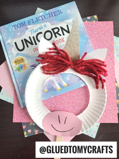 A childrens book titled Theres a Unicorn in Your Book sits beside a unicorn craft made from a paper plate, red yarn, pink paper, and a glittery horn—perfect for fun summer craft ideas! Tag: @GLUEDTOMYCRAFTS.