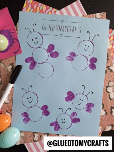A blue paper shows four ladybug drawings made with circles and purple fingerprint wings, created as part of Plastic Egg Stamp Crafts. Each has a smiling face and antennae. The sheet is titled GLUEDTOMYCRAFTS, with a marker and colorful eggs nearby.