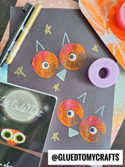 A childrens owl craft made with orange painted circles and googly eyes on black paper, surrounded by markers, a stamp tool, a book titled Little Owls Night, and the text @GLUEDTOMYCRAFTS.