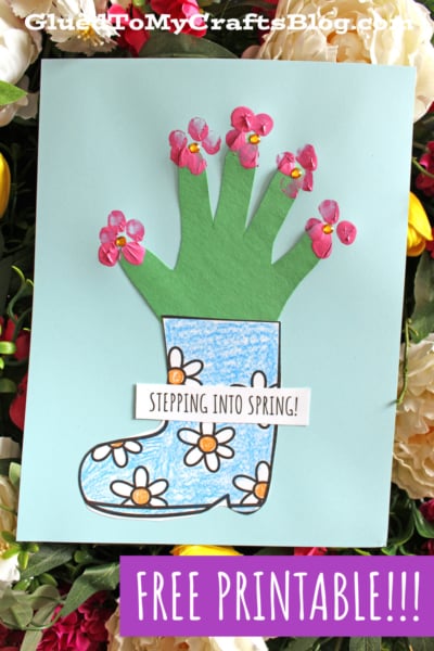 A spring craft featuring a paper cutout of a boot with flowers and a green handprint with flower embellishments as the stems, on a blue background. Text reads, STEPPING INTO SPRING! and FREE PRINTABLE!!!.