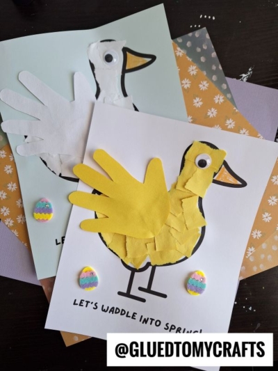 Two spring-themed craft pictures of ducks made from paper handprints, torn paper, and googly eyes, with decorated egg stickers and patterned paper backgrounds. @GLUEDTOMYCRAFTS watermark in the bottom right corner.