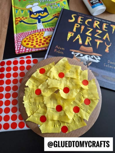 A paper plate craft resembling a pizza with yellow tissue paper cheese and red sticker pepperoni, next to red dot stickers and two childrens books about pizza. @GLUEDTOMYCRAFTS is written at the bottom.