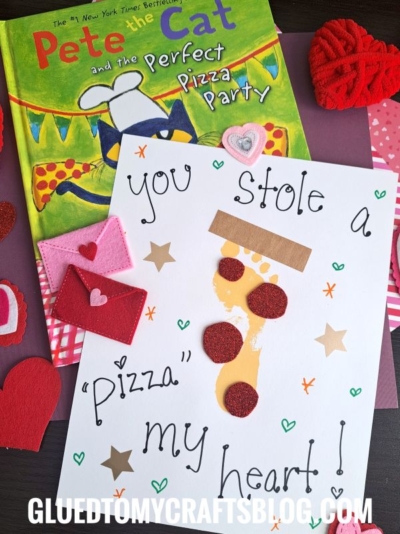 A handmade Valentines card with You stole a pizza my heart! written on it, featuring a pizza slice made of craft materials, sits next to the book Pete the Cat and the Perfect Pizza Party and HANDPRINT FATHER'S DAY-inspired felt hearts.