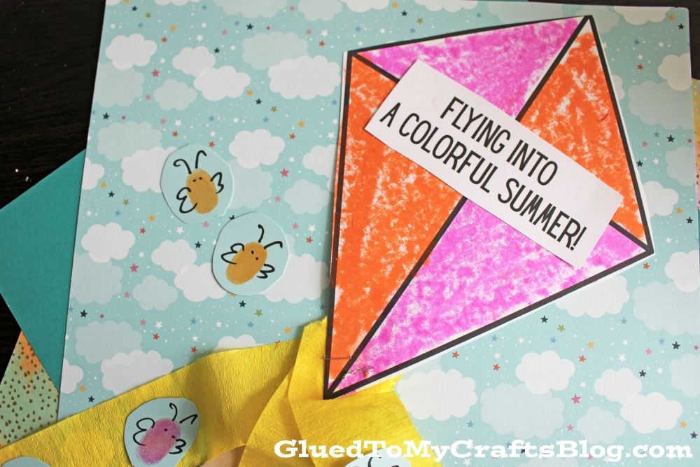 A colorful paper kite with FLYING INTO A COLORFUL SUMMER! written on it is placed on a sky-themed background with clouds and bees. The kite has a yellow ribbon tail with hearts.