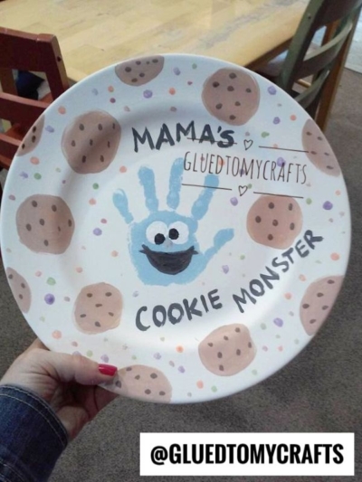 A painted plate with cookie designs, a blue handprint made to look like Cookie Monster, and the words Mamas Cookie Monster in black marker—perfect for Mother's Day keepsakes. The Instagram handle @GLUEDTOMYCRAFTS is displayed at the bottom.