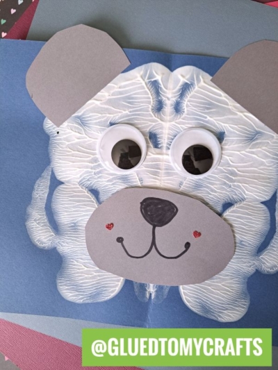 A handmade PAINT SPLAT CRAFTS dog features a white paint blot for the face, large googly eyes, gray paper ears and snout, a drawn smile, and red cheeks. The image includes the text @GLUEDTOMYCRAFTS in a green box at the bottom.