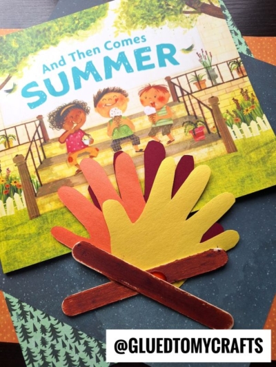 A children's book titled And Then Comes Summer is displayed with colorful paper cutouts of hand shapes and craft sticks arranged to resemble a campfire, perfect for summer craft ideas. @GLUEDTOMYCRAFTS is watermarked on the image.
