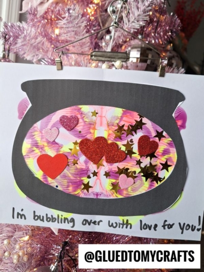 A colorful paper fishbowl craft decorated with red hearts and star-shaped sequins hangs on a pink Christmas tree. Below, handwritten text reads Im bubbling over with love for you!.