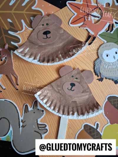 Two bear crafts made from painted coffee filters and paper, reminiscent of a paper plate three little bears theme, are displayed with cutouts of woodland animals and autumn leaves on an orange background. @GLUEDTOMYCRAFTS is labeled at the bottom and multiple places on the image.