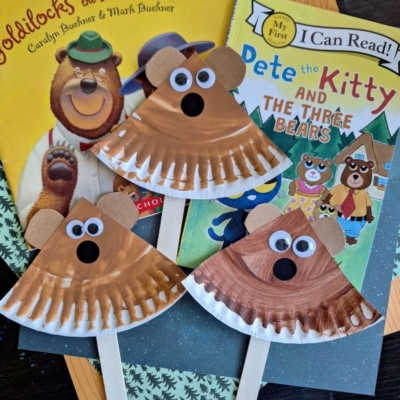 Three bear crafts made from paper plates, googly eyes, and craft sticks are displayed on top of the books Goldilocks and the Three Bears and Pete the Kitty and the Three Bears. A @GLUEDTOMYCRAFTS watermark is shown.