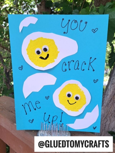 A blue sponge painted egg card features two smiling cracked egg designs made of yellow and white paper, with handwritten text saying You crack me up! and small hearts. Trees and leaves are visible in the background.