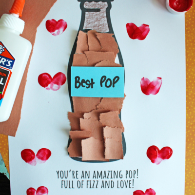 A craft project featuring a paper soda bottle decorated with brown paper squares, a blue label reading “Best Pop,” and red heart stamps. Text below says, Youre an amazing pop! Full of fizz and love! with “Free Printable!!!” banner.
