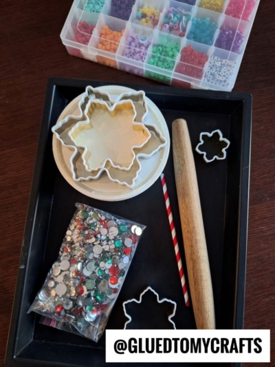 A tray holds snowflake cookie cutters, a rolling pin, a straw, a plate, a bag of colorful rhinestones, and a box of assorted beads. @GLUEDTOMYCRAFTS is written at the bottom.