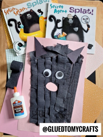 A fun crepe paper craft idea: a cat made from black crepe paper strips, googly eyes, and paper shapes sits on pink paper with glue nearby. Two Splat the Cat books add inspiration in the background.