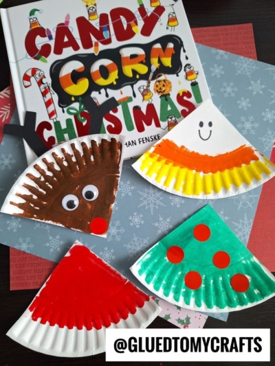 A children’s book titled Candy Corn Christmas with four paper plate crafts: a brown reindeer, a smiling candy corn, a red watermelon slice, and a green Christmas tree. @gluedtomycrafts is written at the bottom.