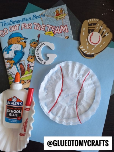 Children’s baseball-themed craft materials: a Berenstain Bears book, a wooden baseball glove, Elmer’s glue, coffee filter crafts for kids like a paper plate decorated as a baseball, and a tag reading “@GLUEDTOMYCRAFTS.”.