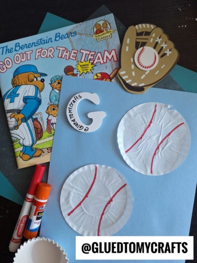 A Berenstain Bears book, a paper baseball glove, markers, glue, cupcake liner card crafts decorated as baseballs, and craft supplies on a blue surface with @GLUEDTOMYCRAFTS text at the bottom.