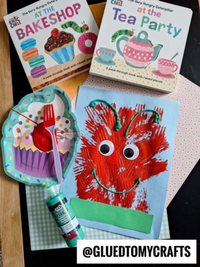 Children’s crafting scene with a cupcake paper plate, green paint bottle, and a HUNGRY CATERPILLAR CRAFT featuring googly eyes. Two Eric Carle books—The Bakeshop and At the Tea Party—are shown. @GLUEDTOMYCRAFTS watermark at the bottom.