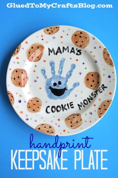 A white plate features chocolate chip cookie designs, a blue handprint cookie monster with googly eyes and a smile, and the text Mamas Cookie Monster. Text below reads handprint keepsake plate.