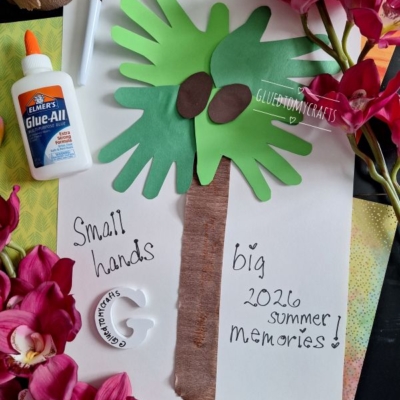 A palm tree craft made with green handprints for leaves and brown paper for the trunk is surrounded by pink flowers, a bottle of glue, and a marker. Text reads, “Small hands big 2026 summer memories!”.