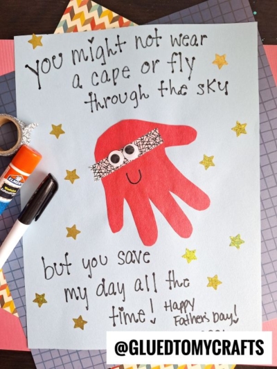 A handmade HANDPRINT FATHER'S DAY card featuring a red handprint shaped like a superhero, with googly eyes and a mask. The card reads: You might not wear a cape or fly, but you save my day! Gold stars are scattered around.