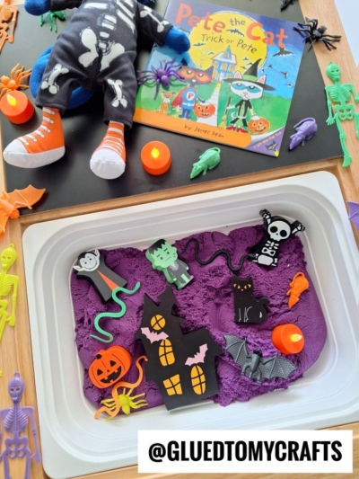 A Halloween-themed sensory bin with purple kinetic sand, foam shapes of a haunted house, pumpkin, skeleton, Frankenstein, bat, plastic bugs, and skeletons. Great for kinetic sand play ideas! Pete the Cat: Trick or Pete is in the background.