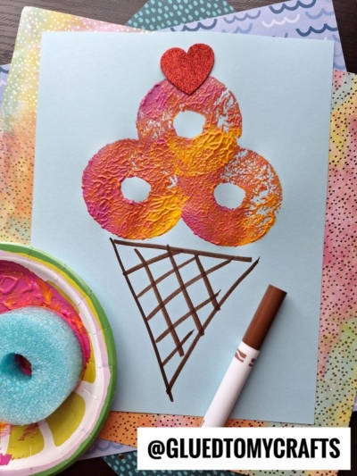 A kids craft depicts ice cream cones made with textured, painted donuts and a red glitter heart on top.