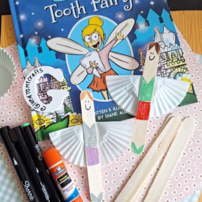 A children’s book titled “An Unfold Story of the Tooth Fairy” is surrounded by craft supplies: markers, glue stick, wooden craft sticks decorated as fairies, cupcake liners, and a @GLUEDTOMYCRAFTS handle.