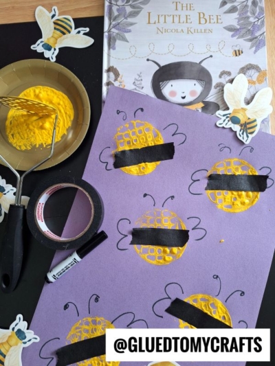 A purple craft paper with yellow sponge-painted bees, black tape for stripes, and drawn antennae. Art supplies, tape, paint, and a bee-themed children’s book are also shown. @GLUEDTOMYCRAFTS is displayed at the bottom.