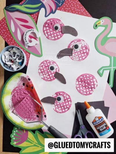 A craft setup featuring five pink bird prints on paper, made using a painted bubble wrap stamp. Nearby are googly eyes, scissors, glue, paper cutouts, and a flamingo illustration. The handle @GLUEDTOMYCRAFTS is shown.