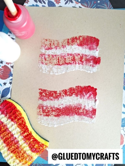 Two red and white striped prints on brown paper made with a yellow, red, and black sponge; a pink paint bottle and white glue bottle are nearby. @GLUEDTOMYCRAFTS is written at the bottom.