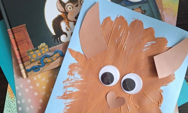 A children’s book titled UNDERWEARWOLF is shown with a handmade brown wolf craft featuring googly eyes on blue paper. Various colored papers are beneath the book and craft. Text reads @GLUEDTOMYCRAFTS.