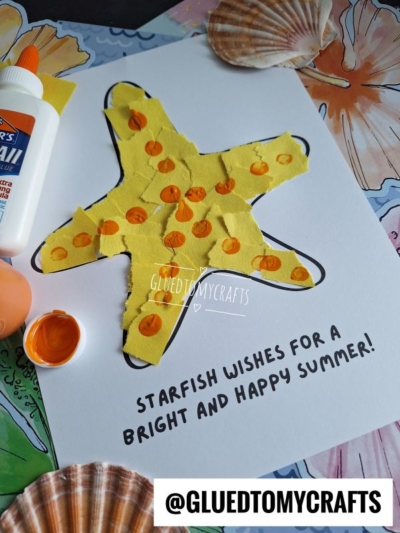 A yellow paper starfish with orange spots is glued onto a paper with the text Starfish wishes for a bright and happy summer! Paint, glue, and seashells are nearby on a decorated surface.