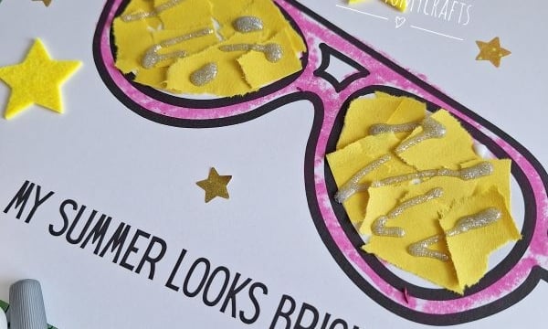 A handmade card features large, colorful sunglasses with yellow lenses decorated with silver glitter. The text reads MY SUMMER LOOKS BRIGHT! Yellow star stickers and craft supplies surround the card.