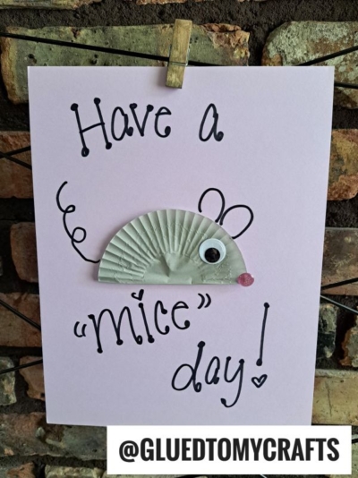 A handmade cupcake liner card features a mouse crafted from a folded liner, a googly eye, and a pink pompom nose. The card reads Have a mice day! with @GLUEDTOMYCRAFTS below—perfect for fans of card crafts.
