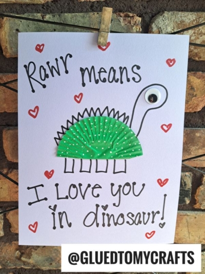 A handmade cupcake liner card features a dinosaur made from a green cupcake liner and a googly eye. The text says, Rawr means I love you in dinosaur! with red hearts. Perfect for cupcake liner card crafts. @GLUEDTOMYCRAFTS is at the bottom.