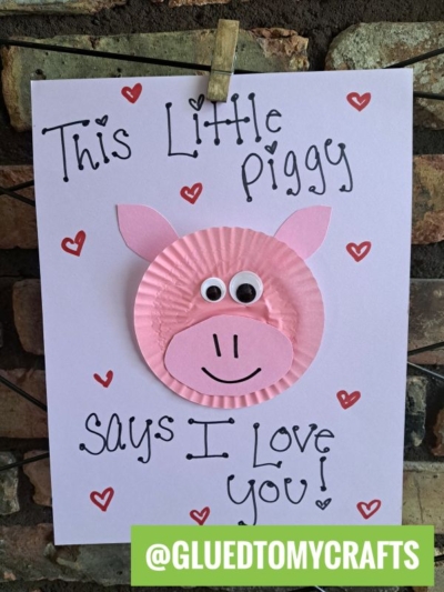 A handmade cupcake liner card features a pink pig face, googly eyes, and a smile. The card reads “This Little Piggy Says I Love You!” with red hearts—perfect for cupcake liner card crafts. @GLUEDTOMYCRAFTS is written at the bottom.