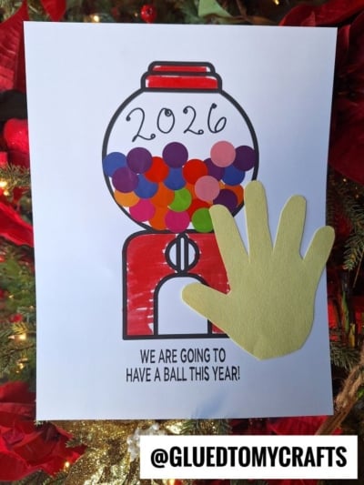 A colorful gumball machine drawing with “2026” written on it, filled with paper circles and a yellow paper handprint on the side. This fun gumball craft idea features the text, “We are going to have a ball this year!” below.
