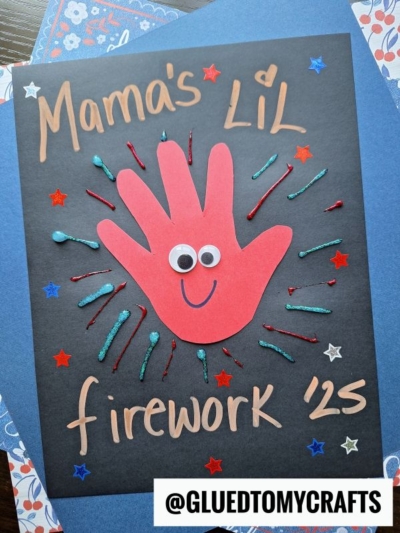 A handmade 4th of July keepsake features a red paper handprint with googly eyes and a smile, surrounded by glitter lines and star stickers on black paper. The text reads “Mama’s Li’l firework ‘25” with a @GLUEDTOMYCRAFTS label.