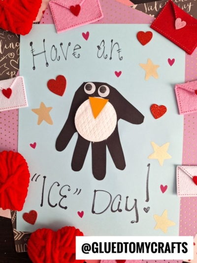 A handmade HANDPRINT FATHER'S DAY card featuring a black handprint penguin with an orange beak, googly eyes, and red hearts. It says, Have an ICE Day! Surrounded by small felt hearts and mini felt envelopes.