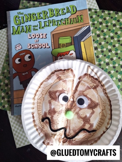 A PAINT SPLAT CRAFT featuring a paper plate with a painted face, googly eyes, green pompom nose, and wavy mouth sits beside The Gingerbread Man and the Leprechaun Loose at School. Green patterned paper forms the background.