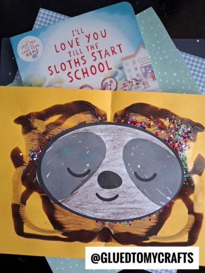 Children’s book Ill Love You Till The Sloths Start School with a sloth-themed craft featuring a smiling paint splat sloth face, brown paint, and colorful glitter on yellow paper. @GLUEDTOMYCRAFTS text is at the bottom.