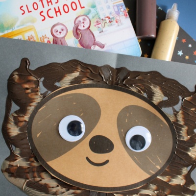 Children’s book and bottles of paint above a paper sloth craft with googly eyes, paint splat textures, and the text “PAINT SPLAT SLOTH” at the bottom.